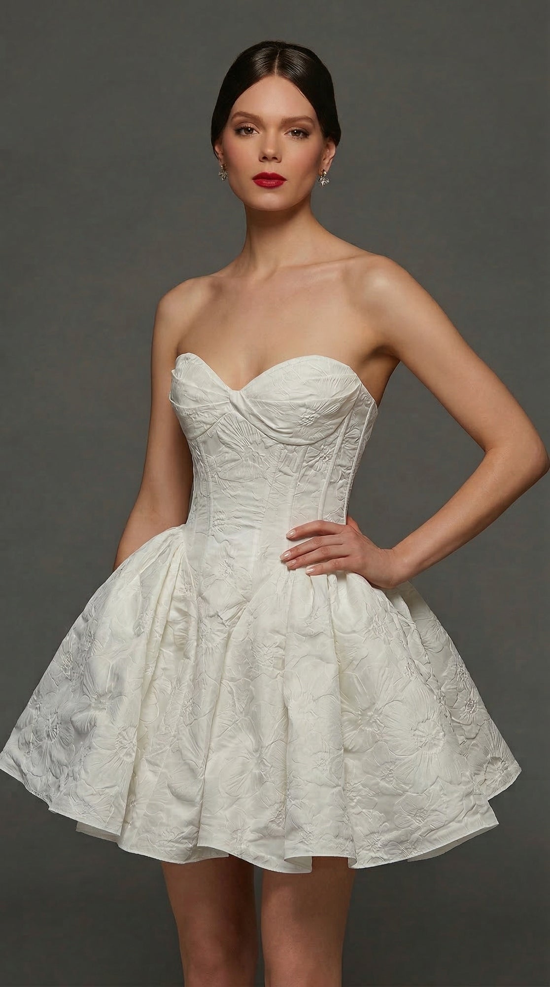 A woman wearing the Alyce 70110 Short White Party Dress in Diamond White, featuring a strapless sweetheart neckline, textured corset bodice, and flared skirt, stands against a plain gray background.
